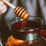 A honey dipper drizzling honey over a steaming coffee carafe in a cozy setting.