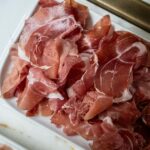 Freshly sliced prosciutto ham served on a white tray in the kitchen.