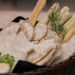 A basket filled with fresh pita, breadsticks, and herbs perfect for meal settings.