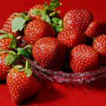 A vivid display of ripe strawberries in a glass bowl on a red fabric background highlighting their freshness.