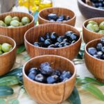 A variety of black and green olives in wooden bowls displayed outdoors, showcasing rustic culinary elegance.