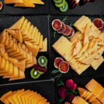 Assorted cheese platters with fruits and garnishes on black slate for gourmet presentation.