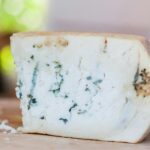 A detailed close-up shot showcasing a wedge of artisan blue cheese with a natural rind on a wooden board.